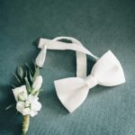 pexels-photo-5037598-5037598 White bow tie and floral boutonniere on textured green fabric, perfect for weddings.
